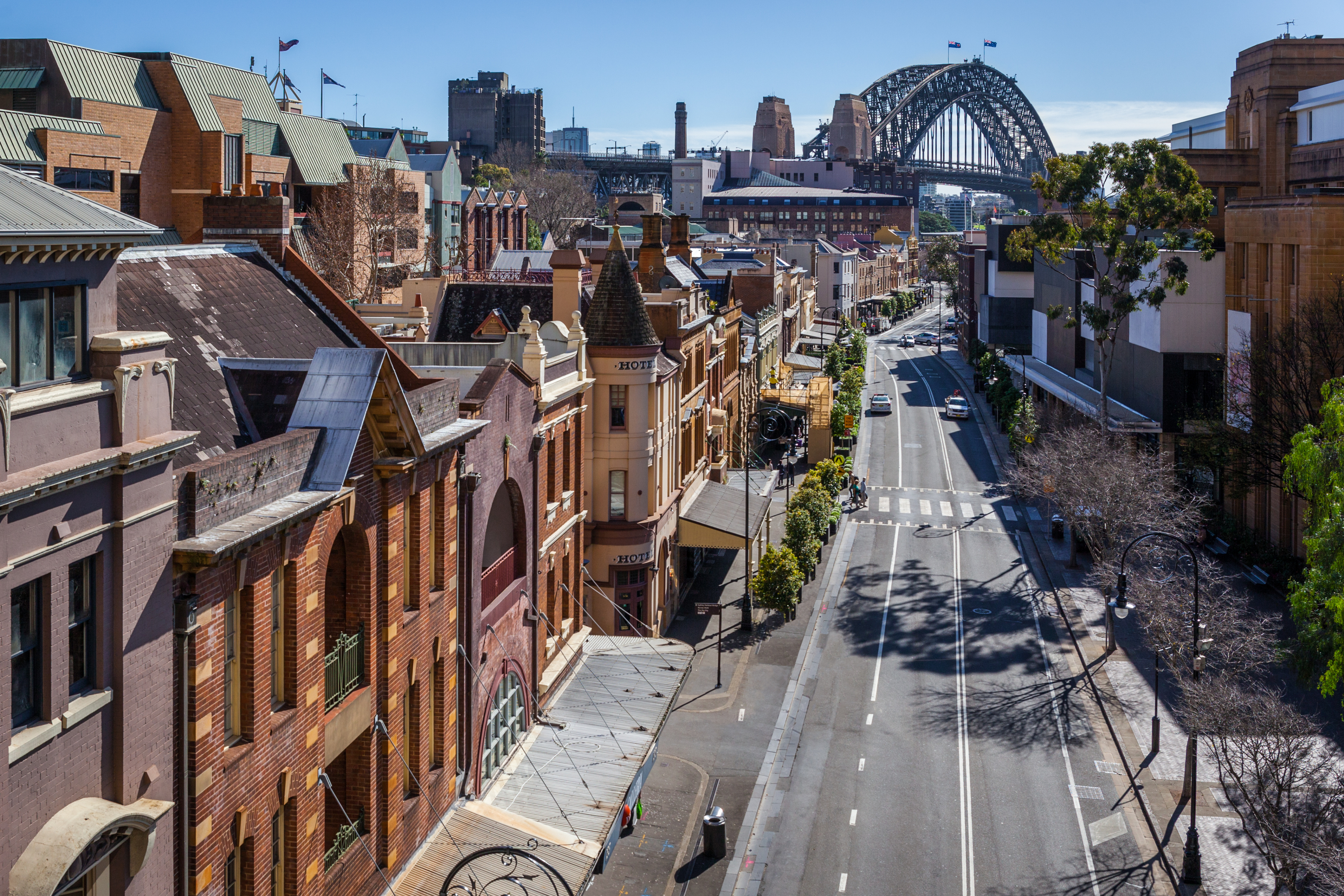 Historic buildings along a quiet street in The Rocks district of Sydney, with the Sydney Harbour Bridge visible in the background