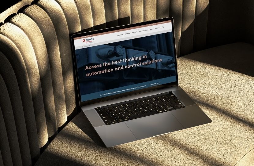 A laptop displaying the SAGE Automation website, sitting on a textured, light brown surface.